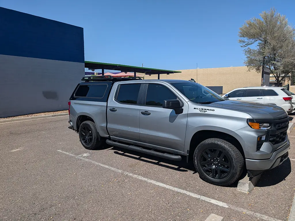 Silver Chevrolet Silverado with a fitted truck cap parked outside Canyon State under a clear blue sky.