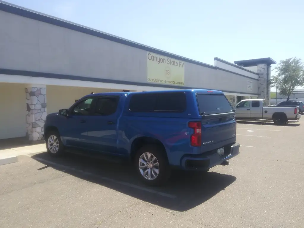 Blue Chevrolet Silverado with a truck cap parked outside Canyon State RV under a sunny sky.