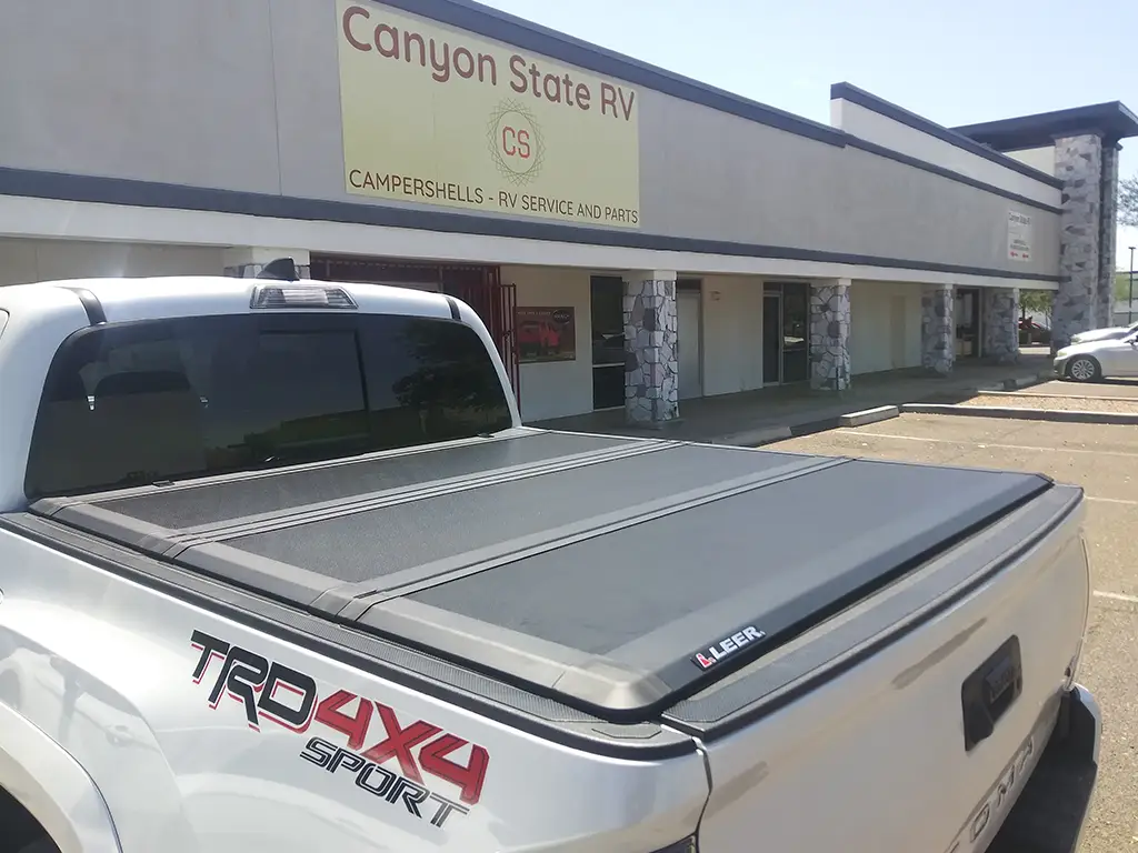 Silver Toyota Tacoma with a LEER folding bed cover, showcased outside Canyon State RV store.