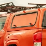Orange truck with a matching truck cap and roof rack, featuring side vent windows, from Canyon State.
