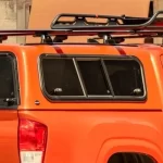 Side window of a Canyon State truck bed cap with a roof rack on an orange truck.