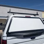 White Ford Super Duty with a Ranch Echo camper shell and Rhino-Rack crossbars.