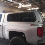 Silver Chevrolet truck with a Ranch Echo camper shell, inside a warehouse.