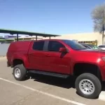 Red lifted truck with a Ranch Echo camper shell parked outside Canyon State RV.