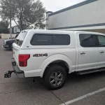 White Ford F-150 with a Ranch Fusion camper shell, parked outside Canyon State RV.