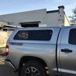 Silver Toyota Tacoma TRD 4x4 with a Ranch Fusion cap parked outside Canyon State RV near a banner display.