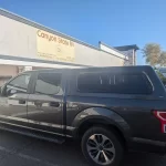 Gray Ford F-150 with a Ranch Fusion camper shell from Canyon State RV, parked outside the store.