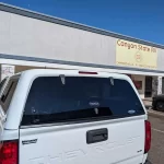White Chevrolet with a Ranch Fusion camper shell from Canyon State RV, parked outside the store.